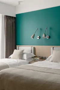 Modern bedroom with twin beds, plush fabric bedding, and a teal accent wall