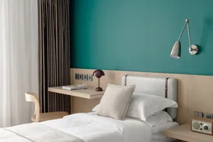 A modern bedroom featuring white furniture, minimalist decor, and a teal accent wall.