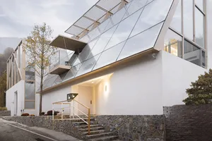 A modern building with a glass exterior and a white facade, featuring a glass roof and large windows.