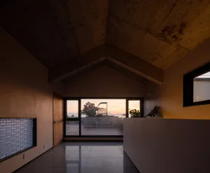 Modern interior with concrete walls and floor, large windows showing a sunset view.