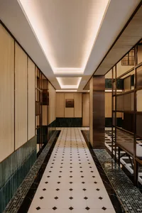 A modern corridor featuring wood walls, metal columns, tiled flooring with a checkered pattern, and glass elements.