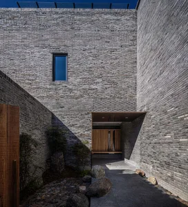 Modern building facade made of grey bricks with a small window and wooden door.