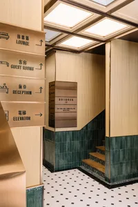 A modern hotel interior with a wooden ceiling, tiled floor, and signage indicating lounge, guest rooms, reception, and lift.