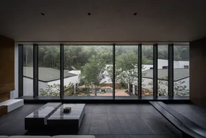 A modern living room featuring a glass wall overlooking a lush green forest.