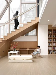 A modern living space featuring light wood floors, minimalist furniture, and a large bookshelf.