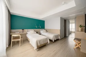 A modern minimalist bedroom with twin beds, wooden headboards, and a green accent wall.