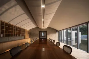 Modern office library with concrete walls and floors, featuring a long wooden table with chairs.