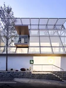 A modern residential building with a glass exterior and a metal lattice roof, featuring a stone staircase leading to an entra