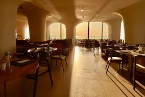 A spacious modern restaurant features stone-floored dining areas with minimalist decor and large windows.