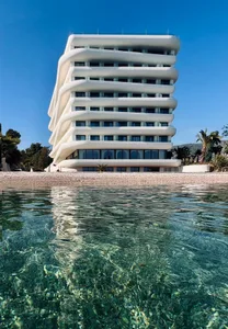 A modern white apartment building with a curved facade overlooking the sea.