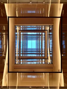 A modern, square-shaped glass staircase with a reflective surface and a repeating pattern of glass and metal frames.