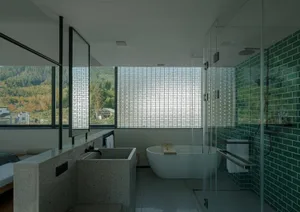 Modern bathroom with concrete walls, glass partition, and porcelain bathtub.