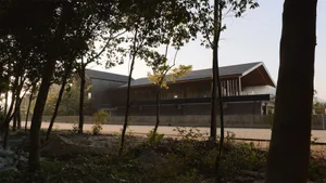 A contemporary restaurant exterior with a wooden frame and glass windows, surrounded by trees and greenery.