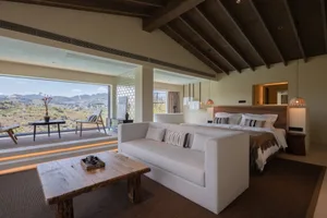 A minimalist bedroom featuring natural textiles, wooden accents, and a glass-enclosed bathroom with a scenic view.