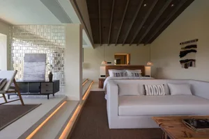 A modern minimalist bedroom featuring a bed with white linens and a white couch, both set against a wooden ceiling with expos