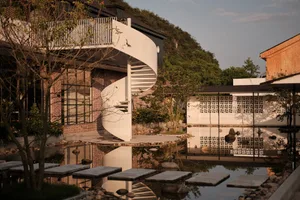 A modern building with brick exterior and spiral staircase surrounded by greenery and water feature.