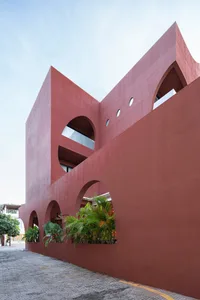 Modern building with a red concrete facade featuring arched windows and balcony.