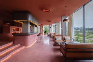 Modern hotel lobby with concrete seating, leather furniture, and large windows overlooking green landscape.
