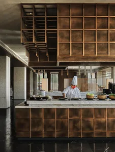 A chef works at a sleek, minimalist kitchen counter featuring wooden panels and marble countertops.