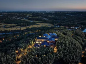 Aerial view of a modern residential building surrounded by greenery and fields at dusk.