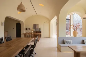 Interior view of a modern restaurant with wooden tables and chairs, concrete flooring, and textile cushions and pillows.