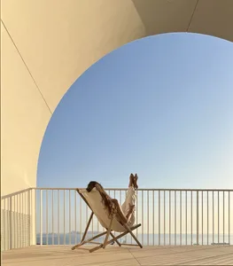 A person relaxing on a deck chair with their feet up on a balcony overlooking the ocean.