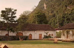A white brick house with clay tiles roof surrounded by trees and mountains.