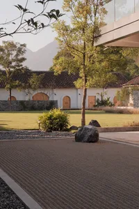 A serene landscape architecture design featuring a gravel pathway, a rock, and lush greenery with a white building in the bac