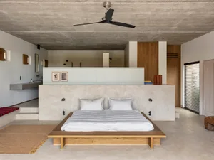A minimalist bedroom with a concrete platform bed, white bedding, and a concrete ceiling.