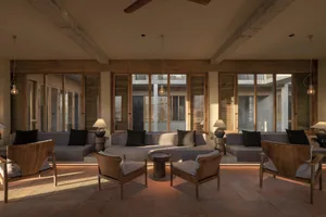 Modern minimalist living room with concrete floors, wooden furniture, and floor-to-ceiling windows.
