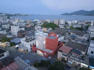 A modern cityscape with a marina in the background, featuring contemporary buildings and a red townhouse.
