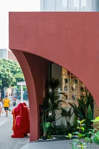 A modern storefront featuring a red concrete structure and lush greenery on a sidewalk.