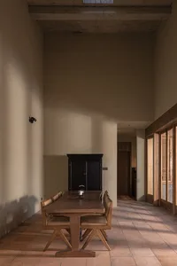 A minimalist dining room featuring a wooden table with chairs and a black cabinet in the background.