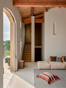 A modern living room with concrete walls and a wooden staircase leading to an upper floor.
