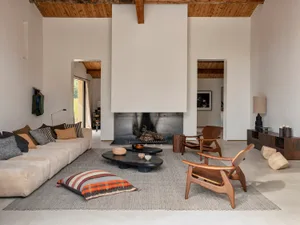 A modern minimalist living room with a wooden beam ceiling, a long sofa, and a fireplace.