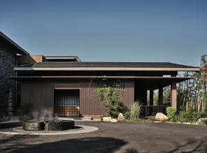 A modern residential building with wooden beam roof and lush greenery around it.