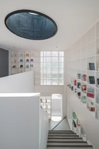 A modern staircase with a bookshelf on a white background, featuring a unique circular skylight.