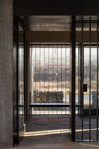 Modern minimalist entrance with glass panels and metal railings overlooking a water body.