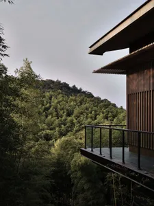 A modern wooden residential structure surrounded by lush greenery and hills.