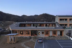A hotel with a wooden exterior and stone walls at night, surrounded by mountains.