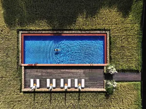 Aerial view of a rectangular swimming pool surrounded by a wooden deck, located within a field of tall grass.