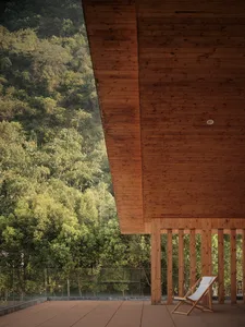 A wooden balcony with a single deck chair overlooking a dense, green forested hillside.