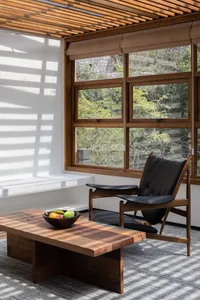Modern living room with white walls, a wooden table, a black leather chair, and a bowl of fruit.