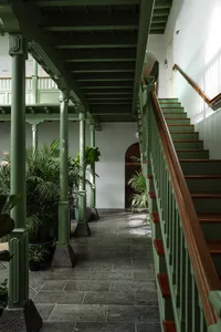 A green-painted corridor with a wooden staircase and metal railings.