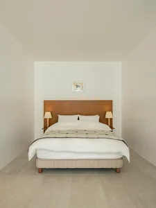 A minimalist bedroom featuring a neutral-toned bed with a simple headboard, side tables with lamps, and a framed picture on t