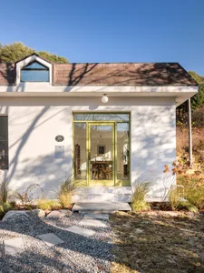 Modern house with concrete exterior, glass door, green accents, and gravel path.