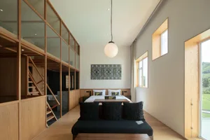 A modern bedroom featuring a bed with a minimalist design, black cushions, and a large window with natural light.
