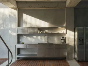A minimalist kitchen with metallic cabinets and shelves, featuring a sink, countertop, and open shelving.