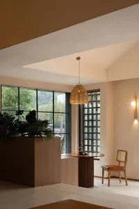 Modern wooden living room with large windows, a rattan pendant light, and a cozy seating area.
