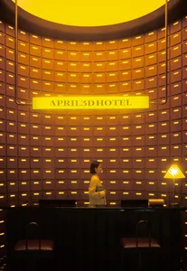 A modern hotel lobby featuring a warm, wooden interior with a reception desk and a yellow light fixture.